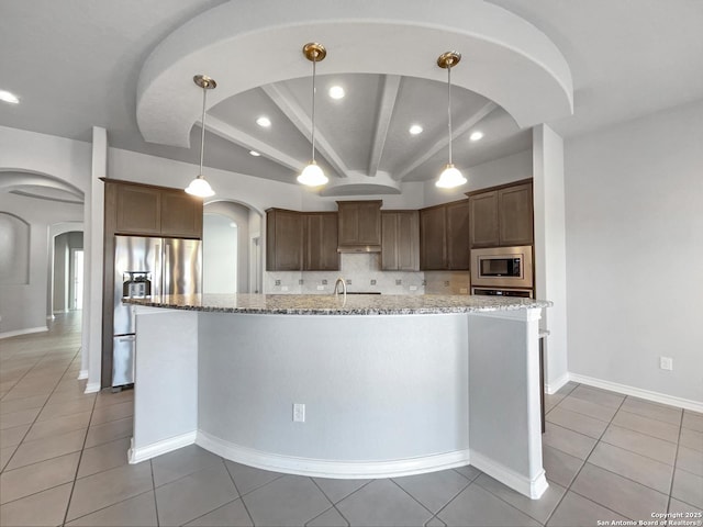 kitchen featuring light stone counters, hanging light fixtures, a center island with sink, and appliances with stainless steel finishes