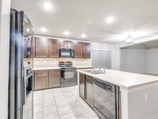 kitchen featuring sink, decorative backsplash, light tile patterned floors, black appliances, and a center island with sink