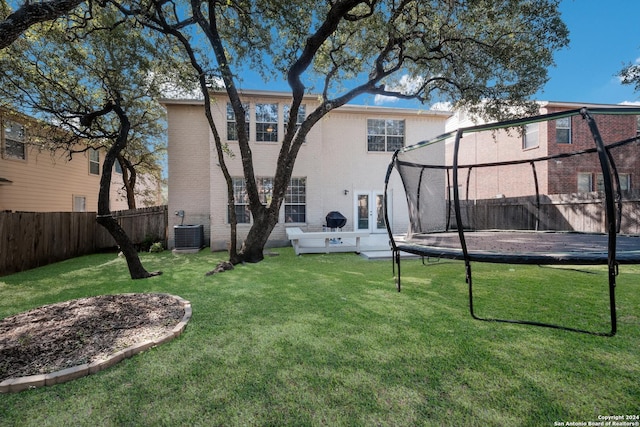 back of property with central AC unit, a trampoline, and a lawn