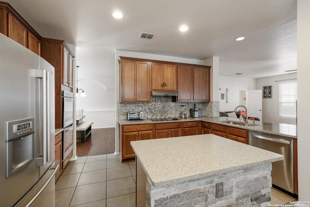 kitchen featuring sink, light stone counters, a center island, kitchen peninsula, and stainless steel appliances