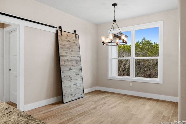 unfurnished dining area featuring an inviting chandelier, a barn door, and light hardwood / wood-style flooring