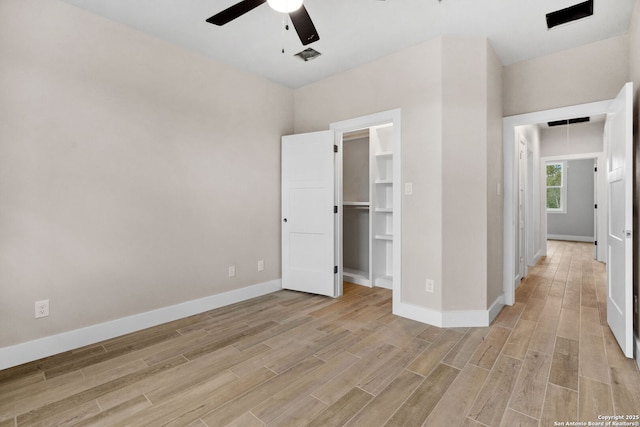 unfurnished bedroom with ceiling fan, a spacious closet, light wood-type flooring, and a closet