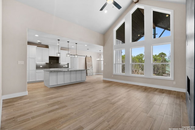 kitchen with tasteful backsplash, white cabinetry, an island with sink, hanging light fixtures, and light hardwood / wood-style floors