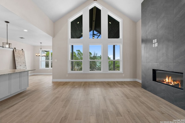 unfurnished living room with an inviting chandelier, a barn door, a towering ceiling, a fireplace, and light hardwood / wood-style floors