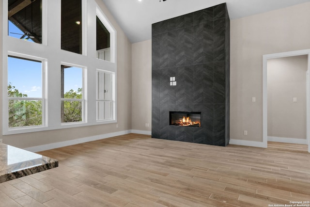 unfurnished living room featuring a towering ceiling, a tiled fireplace, and light hardwood / wood-style floors