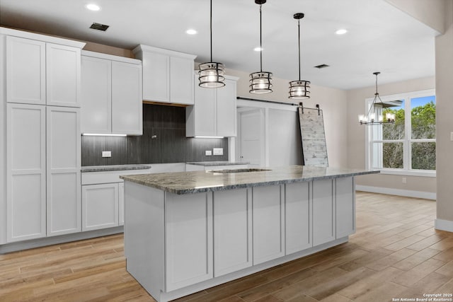 kitchen featuring white cabinetry, a barn door, an island with sink, and decorative light fixtures