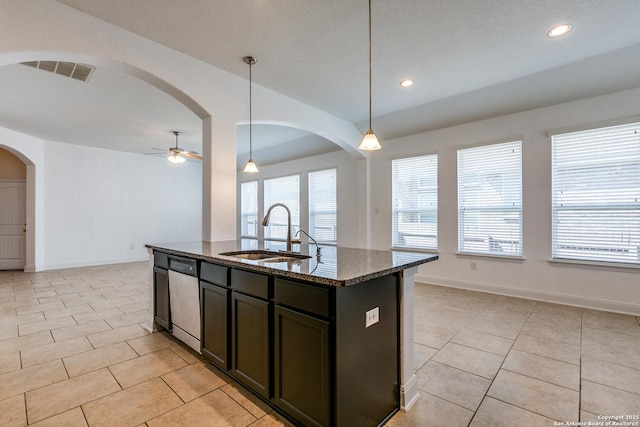 kitchen with sink, decorative light fixtures, a center island with sink, dark stone countertops, and dishwasher