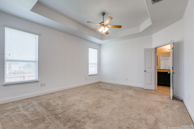 carpeted spare room featuring sink, a tray ceiling, and ceiling fan