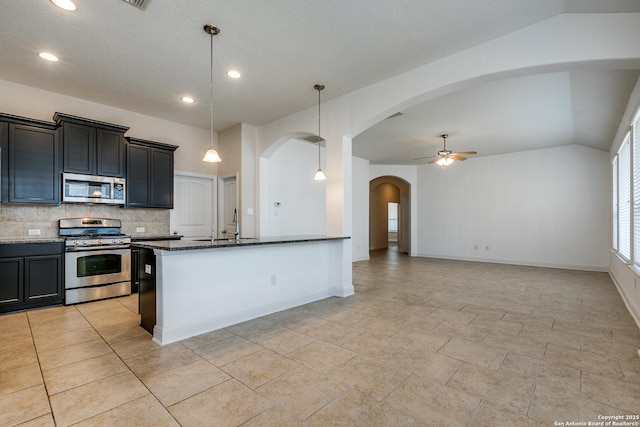 kitchen featuring lofted ceiling, appliances with stainless steel finishes, dark stone countertops, tasteful backsplash, and decorative light fixtures