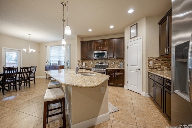 kitchen featuring pendant lighting, sink, appliances with stainless steel finishes, a kitchen island with sink, and light stone countertops