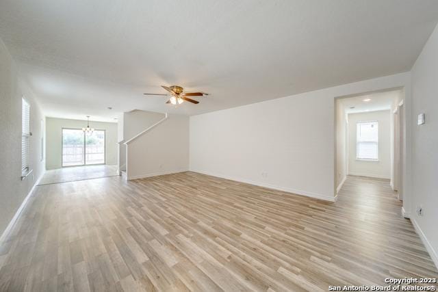 unfurnished living room featuring ceiling fan with notable chandelier, plenty of natural light, and light wood-type flooring