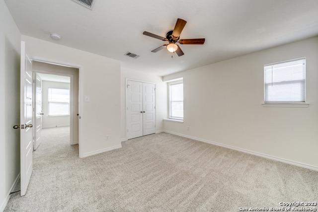 unfurnished bedroom with multiple windows, light carpet, ceiling fan, and a closet