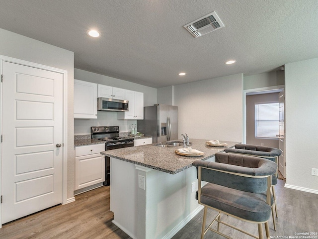 kitchen with stainless steel appliances, light hardwood / wood-style floors, a center island with sink, and white cabinets