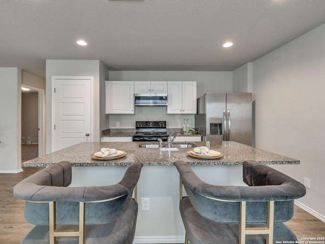 kitchen featuring white cabinetry, a kitchen island with sink, stainless steel appliances, a kitchen breakfast bar, and light stone counters