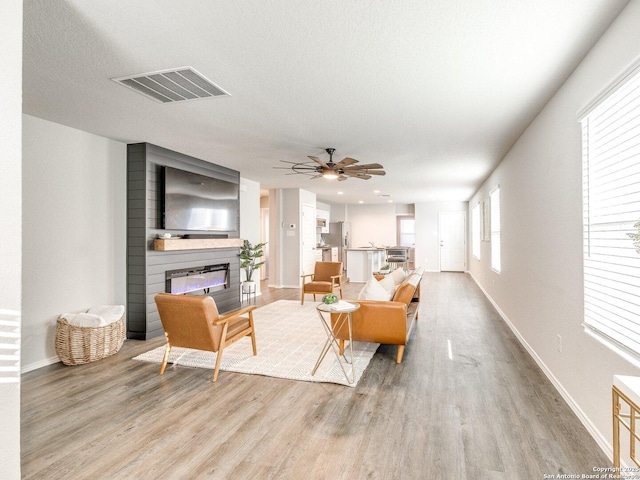 living room featuring ceiling fan, a fireplace, light hardwood / wood-style floors, and a textured ceiling