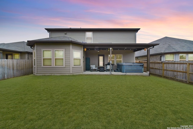 back house at dusk featuring a hot tub, a lawn, and a patio area