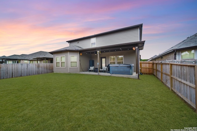 back house at dusk featuring a yard, a patio area, and a hot tub