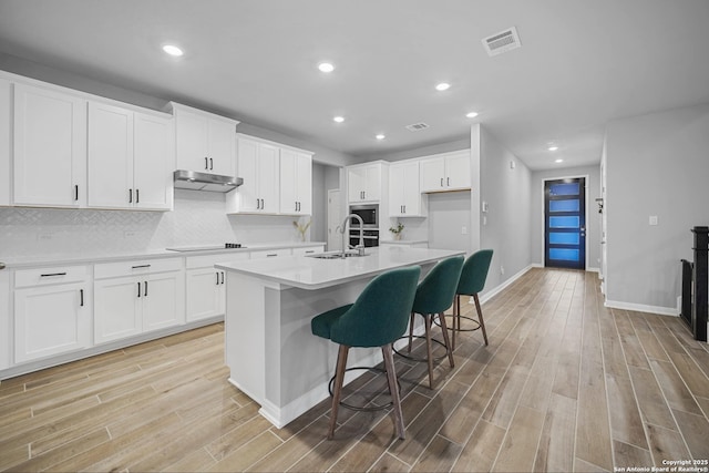 kitchen featuring sink, white cabinetry, stainless steel microwave, a kitchen breakfast bar, and an island with sink