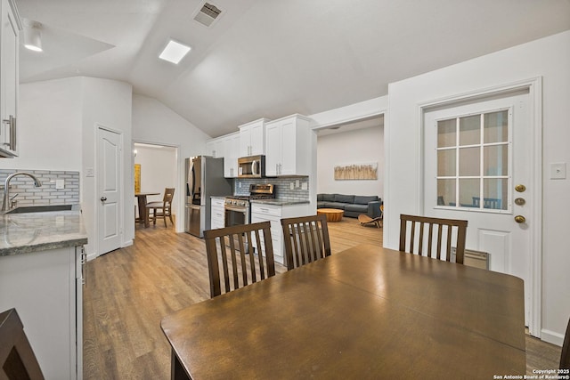 dining area featuring sink, vaulted ceiling, and light hardwood / wood-style floors