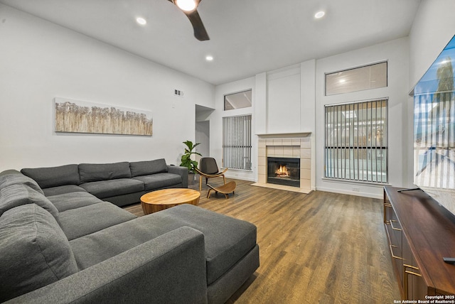 living room featuring a tile fireplace, dark wood-type flooring, and ceiling fan