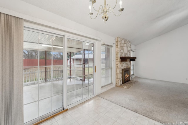 unfurnished living room with a notable chandelier, a stone fireplace, vaulted ceiling, and light colored carpet