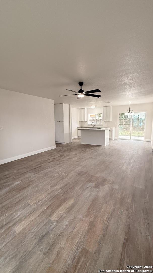 unfurnished living room with ceiling fan with notable chandelier, sink, hardwood / wood-style floors, and a textured ceiling