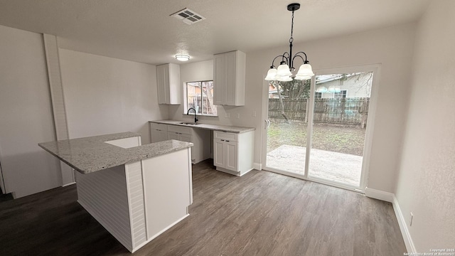 kitchen featuring a kitchen island, white cabinetry, sink, hanging light fixtures, and light stone countertops