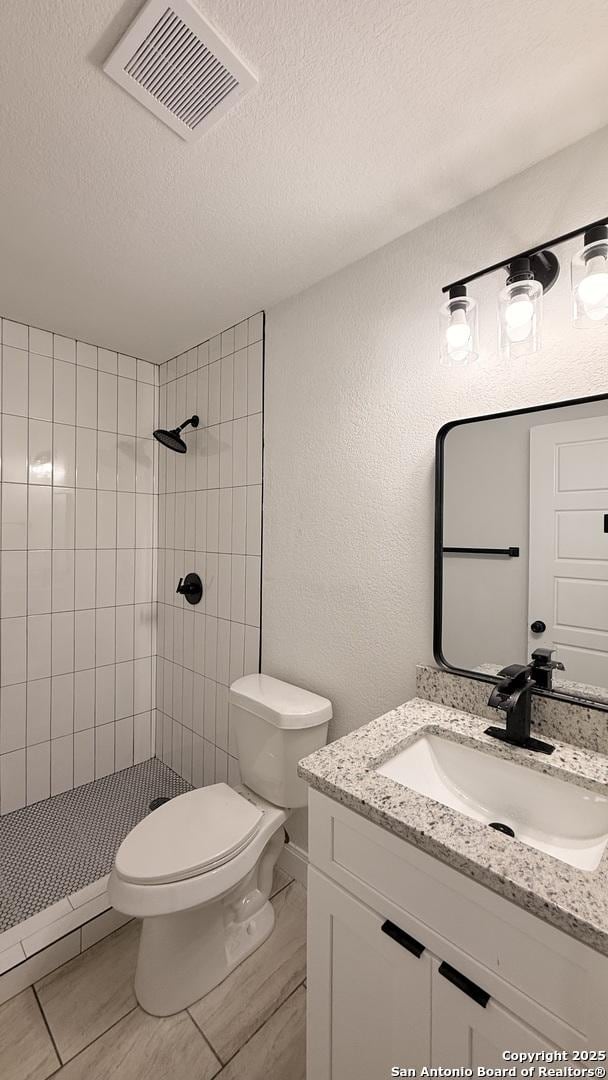 bathroom featuring vanity, tiled shower, a textured ceiling, and toilet