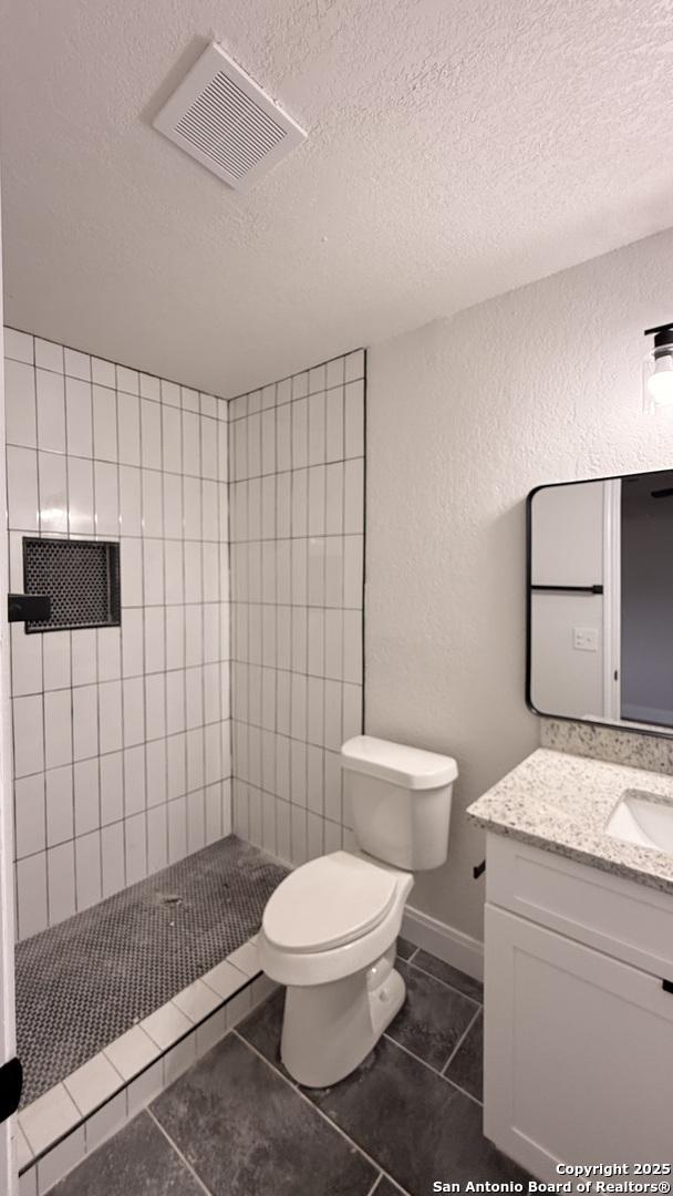 bathroom with tiled shower, toilet, a textured ceiling, vanity, and tile patterned flooring