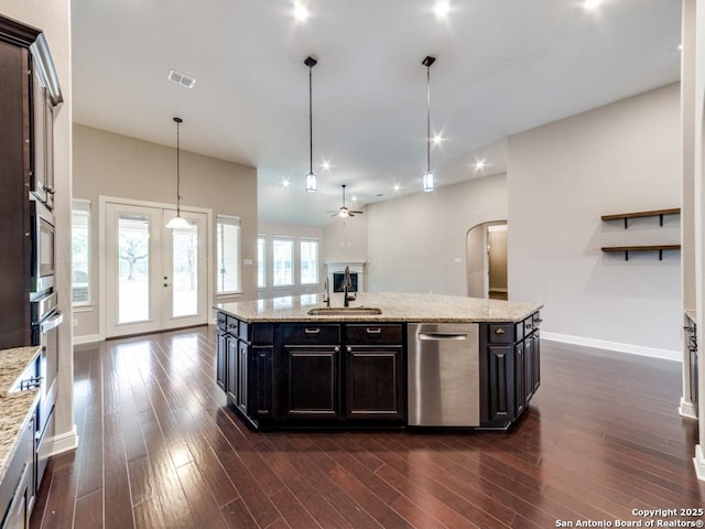 kitchen with sink, light stone counters, dark hardwood / wood-style floors, an island with sink, and pendant lighting