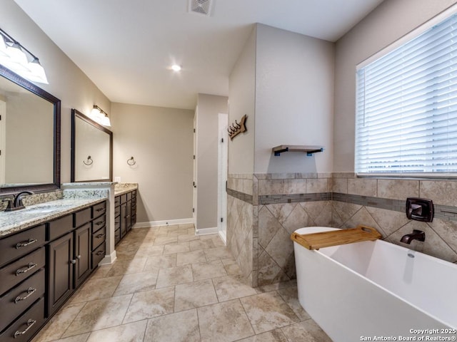 bathroom with a washtub, vanity, tile patterned flooring, and tile walls