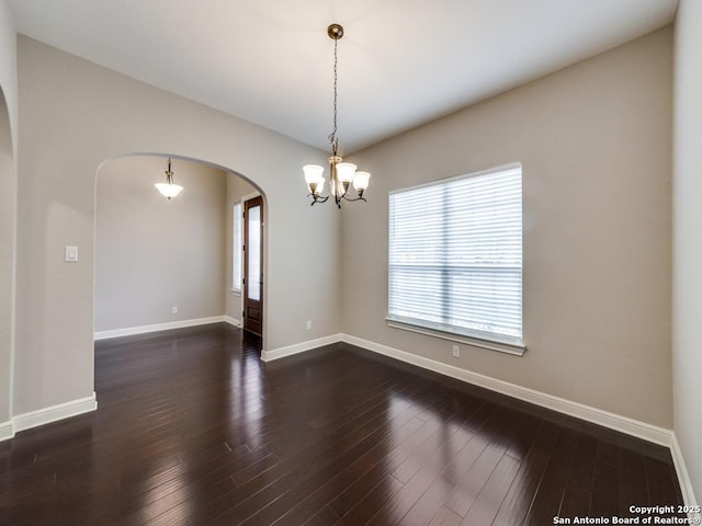 spare room with dark hardwood / wood-style flooring and an inviting chandelier