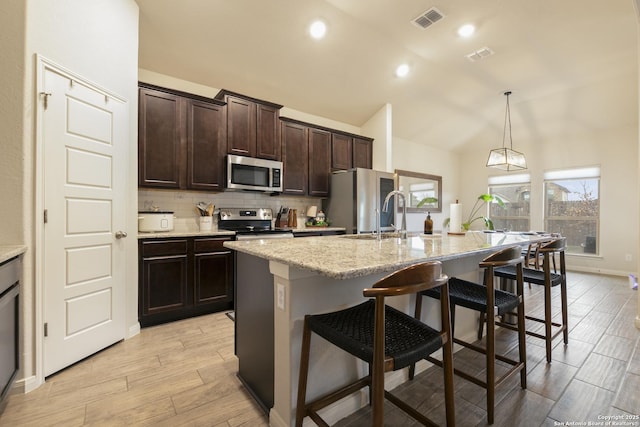 kitchen with tasteful backsplash, an island with sink, appliances with stainless steel finishes, and a breakfast bar area