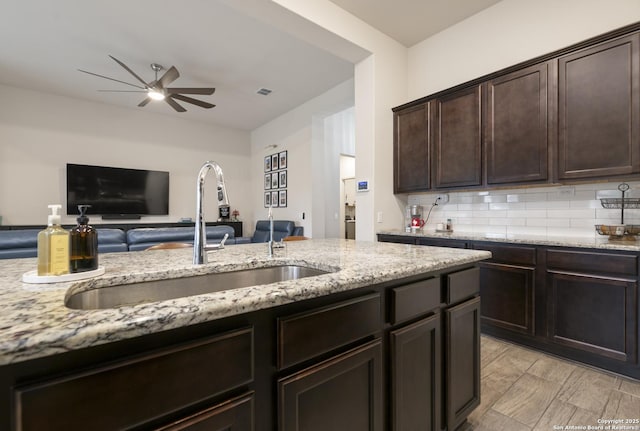 kitchen featuring light stone counters, dark brown cabinets, sink, and decorative backsplash