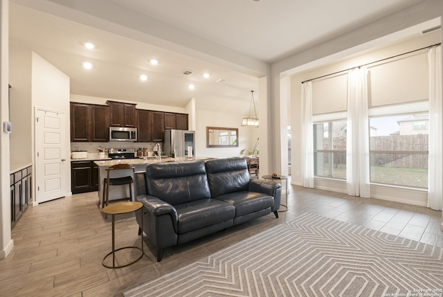 living room featuring light hardwood / wood-style flooring, sink, vaulted ceiling, and an inviting chandelier