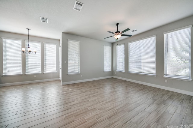 empty room with ceiling fan with notable chandelier, light hardwood / wood-style floors, and a wealth of natural light