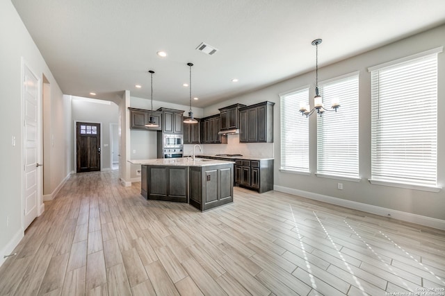 kitchen with pendant lighting, a notable chandelier, a kitchen island with sink, and appliances with stainless steel finishes