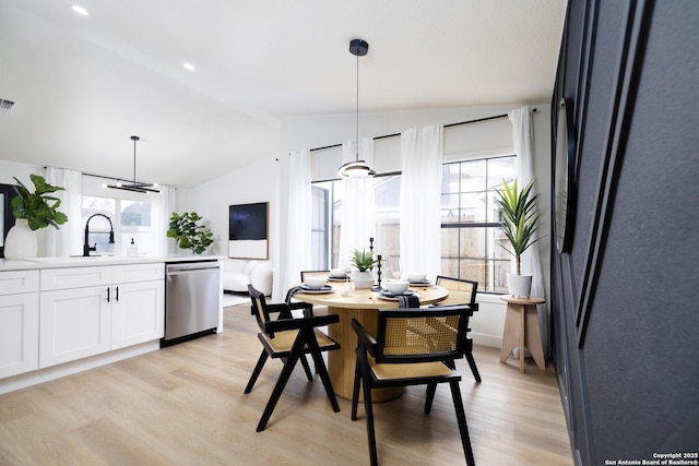 dining space with vaulted ceiling, sink, and light hardwood / wood-style flooring