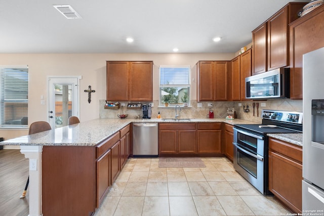 kitchen with appliances with stainless steel finishes, sink, a kitchen bar, kitchen peninsula, and light stone countertops