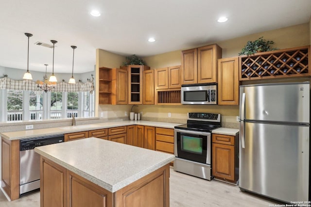 kitchen with appliances with stainless steel finishes, decorative light fixtures, sink, light hardwood / wood-style floors, and kitchen peninsula