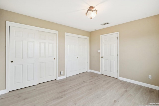 unfurnished bedroom featuring multiple closets and light hardwood / wood-style floors