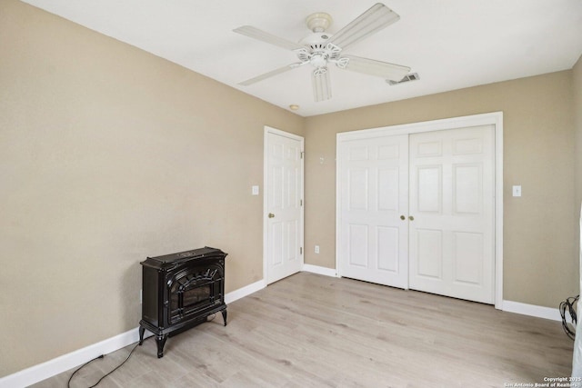 bedroom with ceiling fan, a wood stove, light hardwood / wood-style floors, and a closet