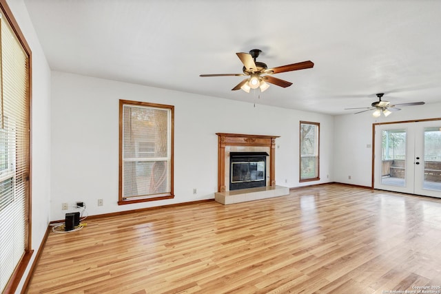 unfurnished living room featuring ceiling fan, a fireplace, light wood-type flooring, and french doors