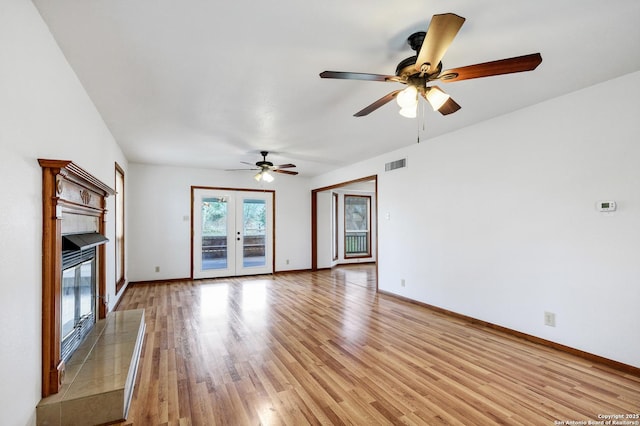 unfurnished living room featuring a tiled fireplace, light hardwood / wood-style flooring, french doors, and ceiling fan