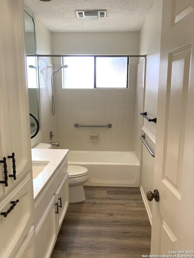 full bathroom featuring tiled shower / bath, wood-type flooring, vanity, toilet, and a textured ceiling