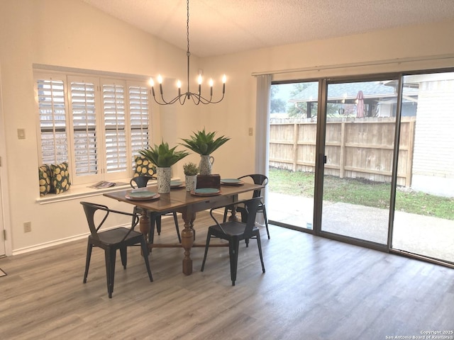 dining area featuring hardwood / wood-style flooring, lofted ceiling, a textured ceiling, and an inviting chandelier