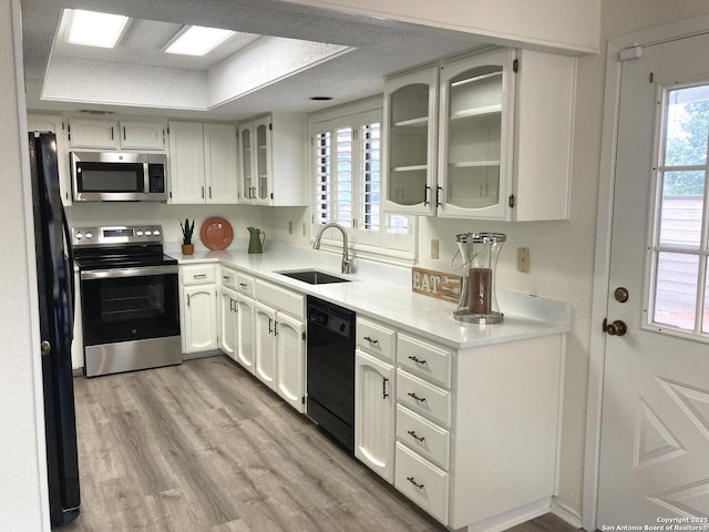 kitchen featuring sink, black appliances, light hardwood / wood-style floors, white cabinets, and a textured ceiling