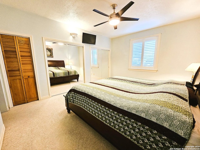 carpeted bedroom with a textured ceiling, a ceiling fan, and two closets