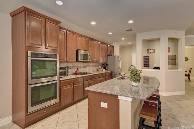 kitchen featuring light tile patterned flooring, sink, a center island with sink, appliances with stainless steel finishes, and a kitchen breakfast bar