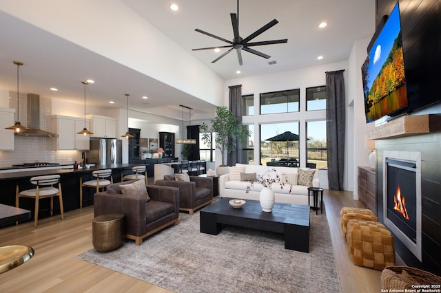 living room featuring a high ceiling, ceiling fan, and light wood-type flooring